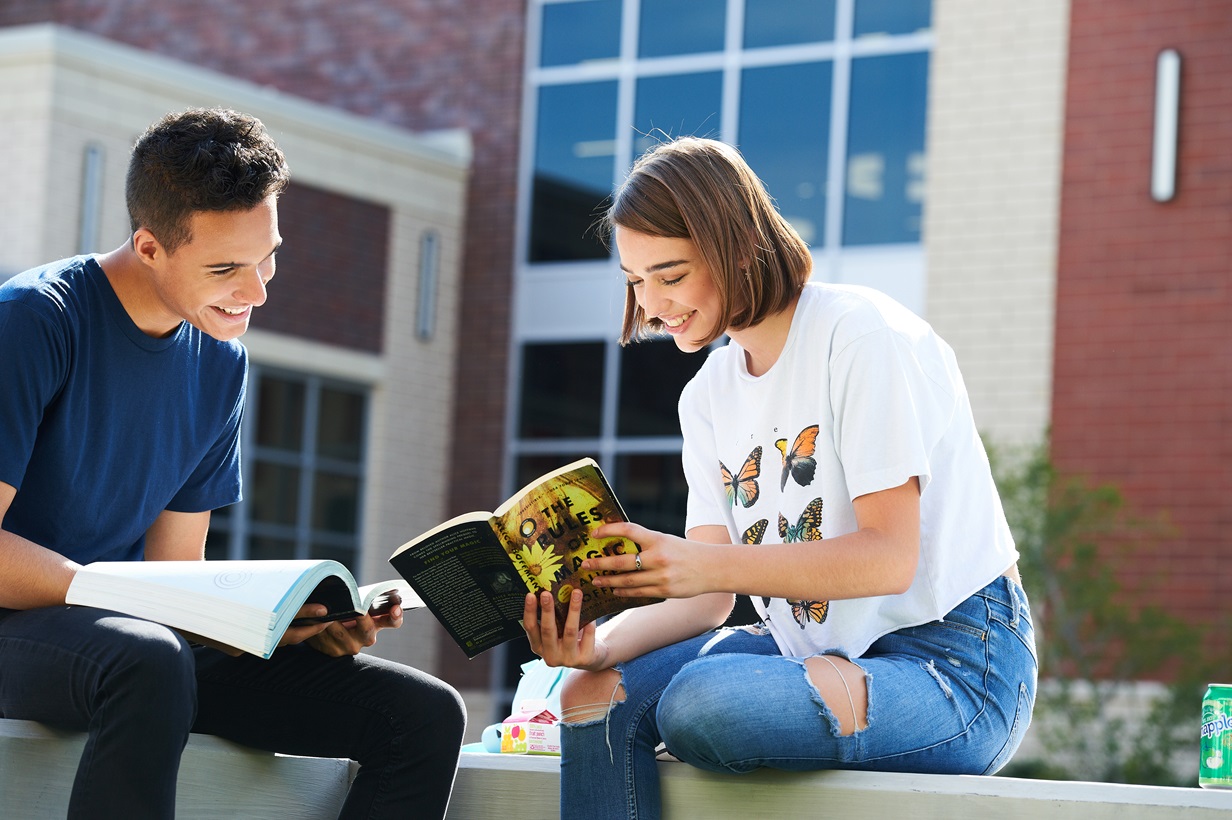 Two students sitting on a bench and reading books.
